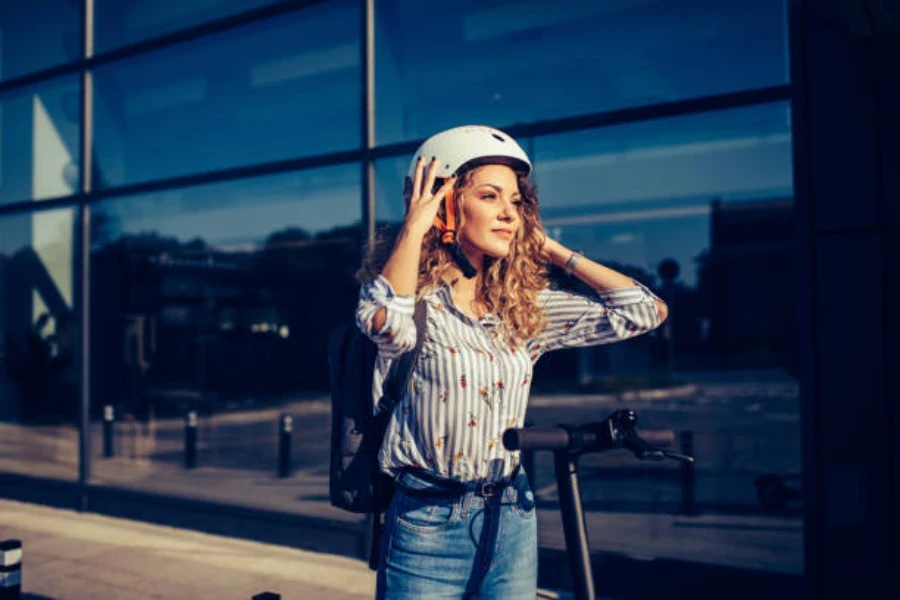 Mujer poniéndose un casco blanco antes de montar en scooter eléctrico