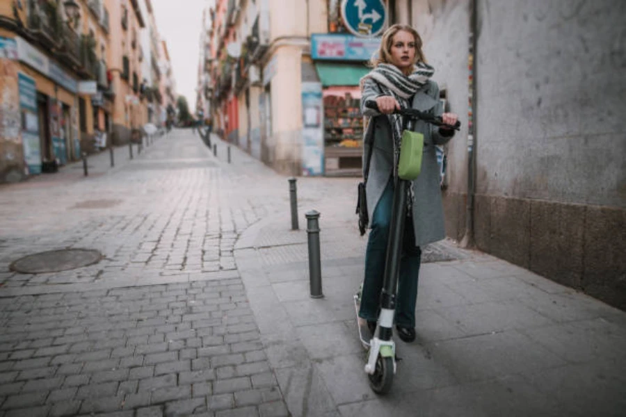 Mujer montando scooter eléctrico con una pequeña bolsa frontal verde