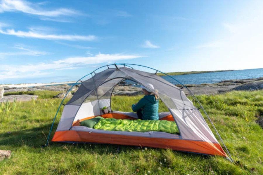 Woman sitting inside tent with view of lake in daytime