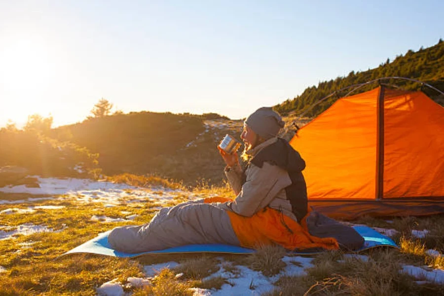 Femme assise sur un tapis de camping avec de la neige autour d'elle