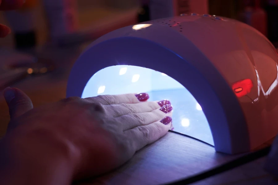 woman’s painted nails under nail lamp