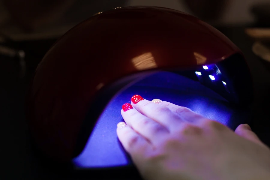Rot lackierte Nägel einer Frau unter einer Nagellampe