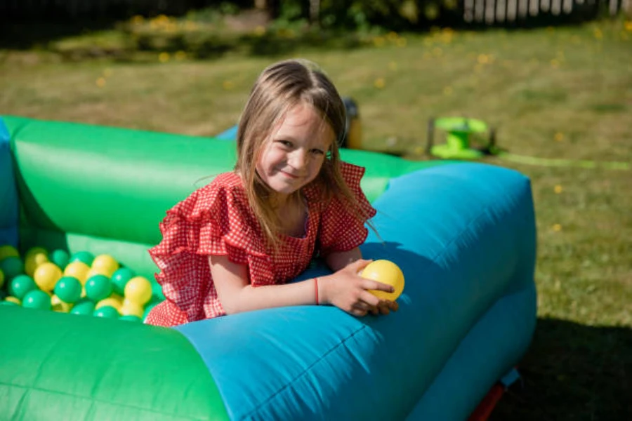 Young girl sitting inside inflatable ball pit in garden