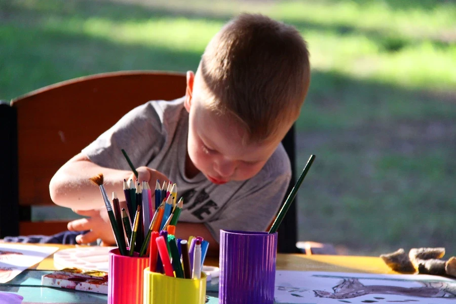 Un niño usando colores y pinturas mientras está sentado afuera.