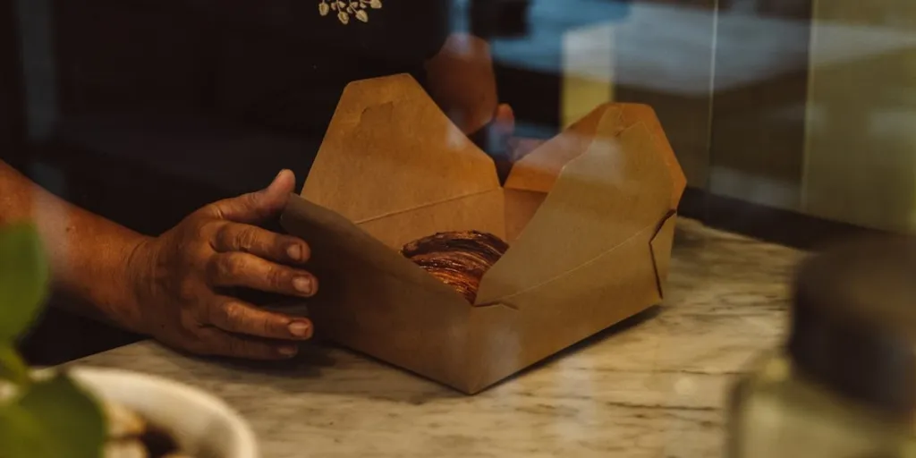 A man with a cardboard takeaway box with a pastry inside