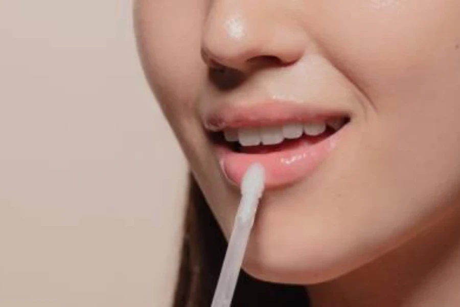 Una joven aplicando brillo de labios sobre un fondo marrón.