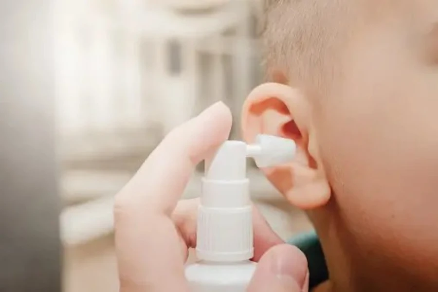Adult spritzing ear spray into a little boy’s ear