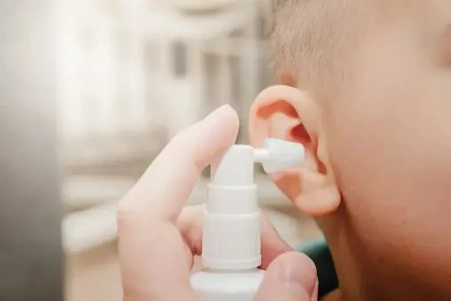 Un adulte vaporise un spray auriculaire dans l’oreille d’un petit garçon