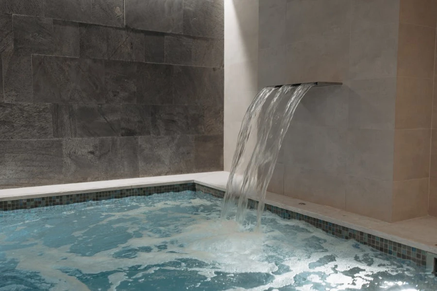 An in-wall pool fountain pouring into an indoor pool