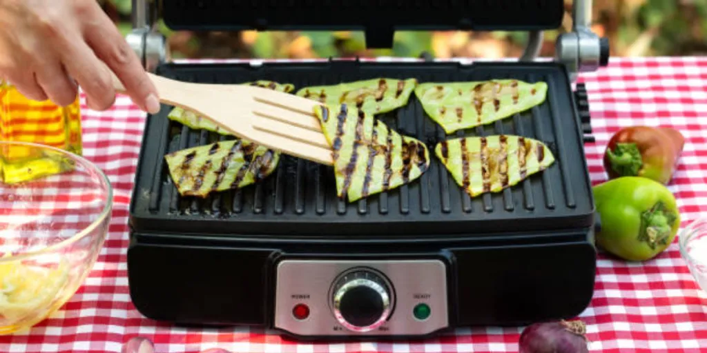 black electric grill with vegetables grilling on picnic table