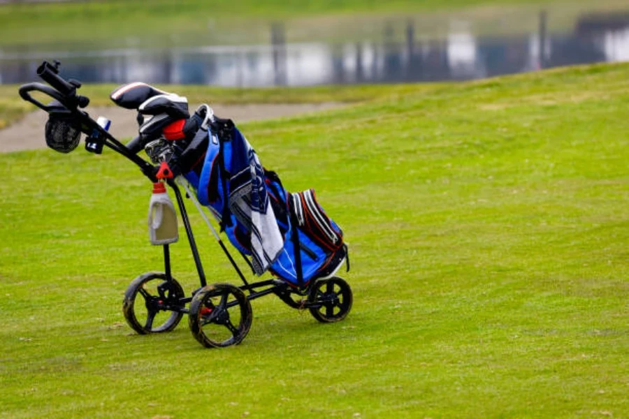 Troli golf hitam memegang tas golf biru dengan tongkat