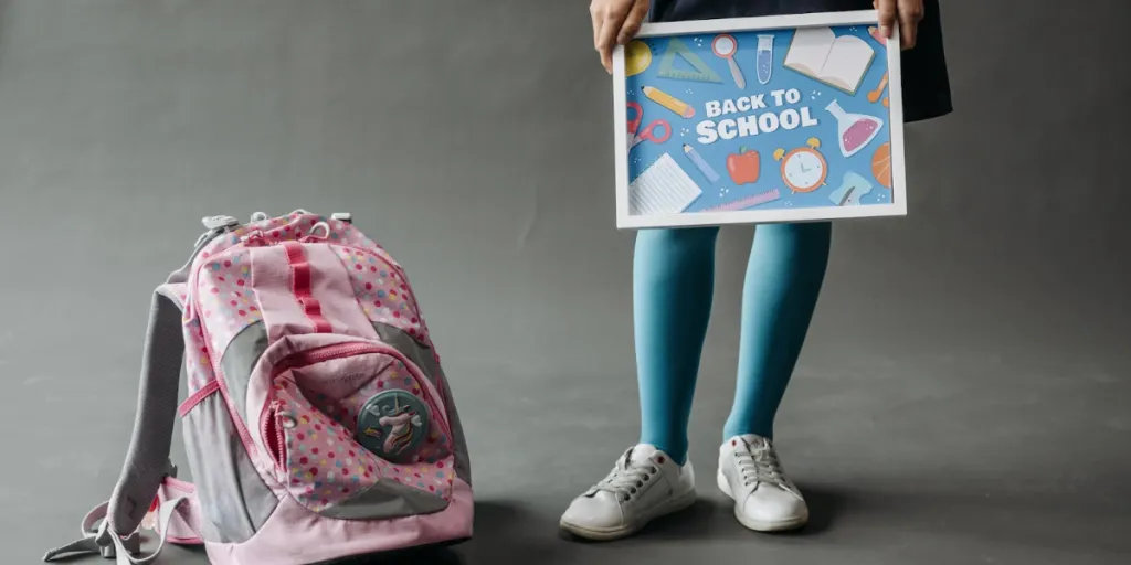 Child holding a Back to School sign standing near a bookbag