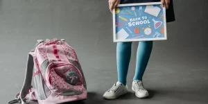 Anak yang memegang tanda Kembali ke Sekolah berdiri di dekat tas buku