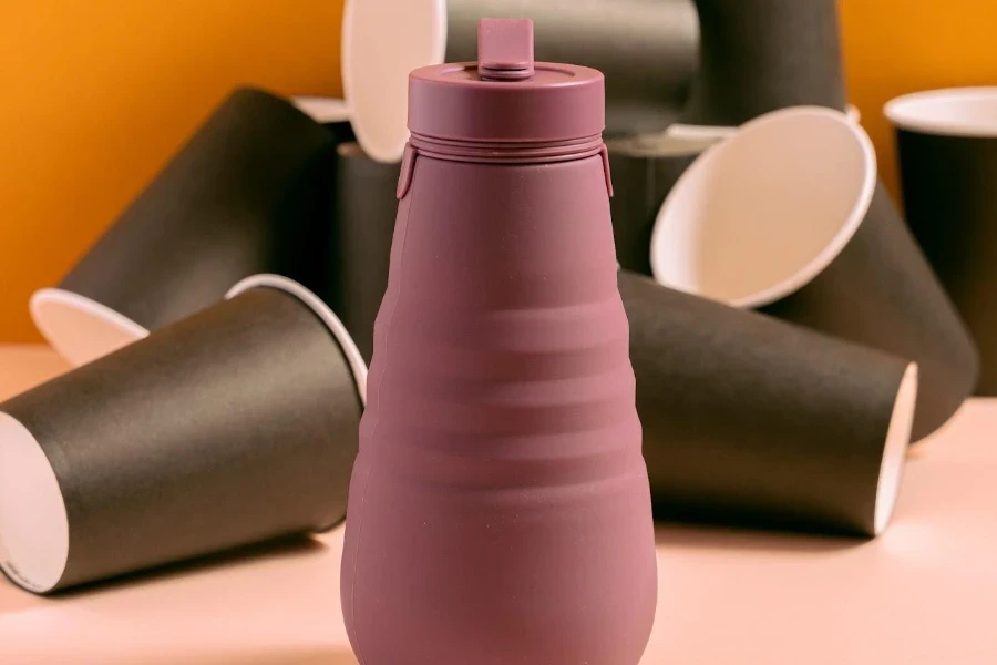 bouteille d'eau de sport pliable avec des gobelets en papier en arrière-plan