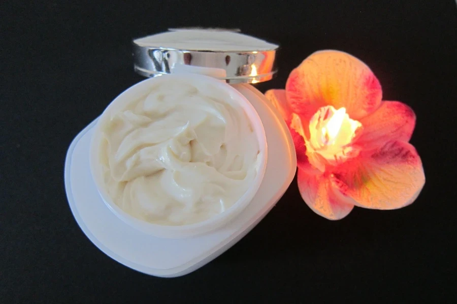 crema en un frasco blanco junto a una vela de flores