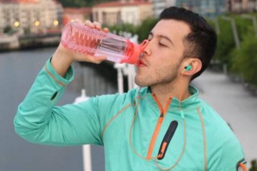 atleta maschio che beve acqua da una bottiglia d'acqua sportiva con paglia