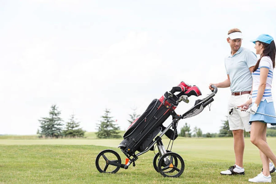 Man and woman walking on green pushing black golf trolley