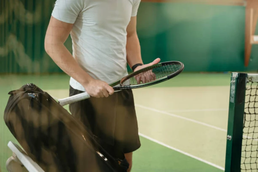 man holding racket next to all black tennis racket bag