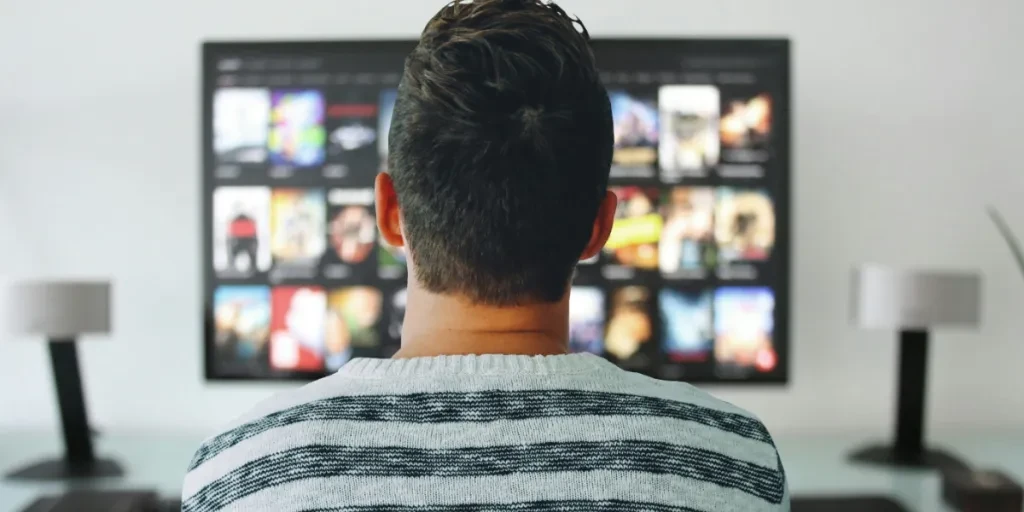 Hombre frente a un televisor con muchas portadas de películas.