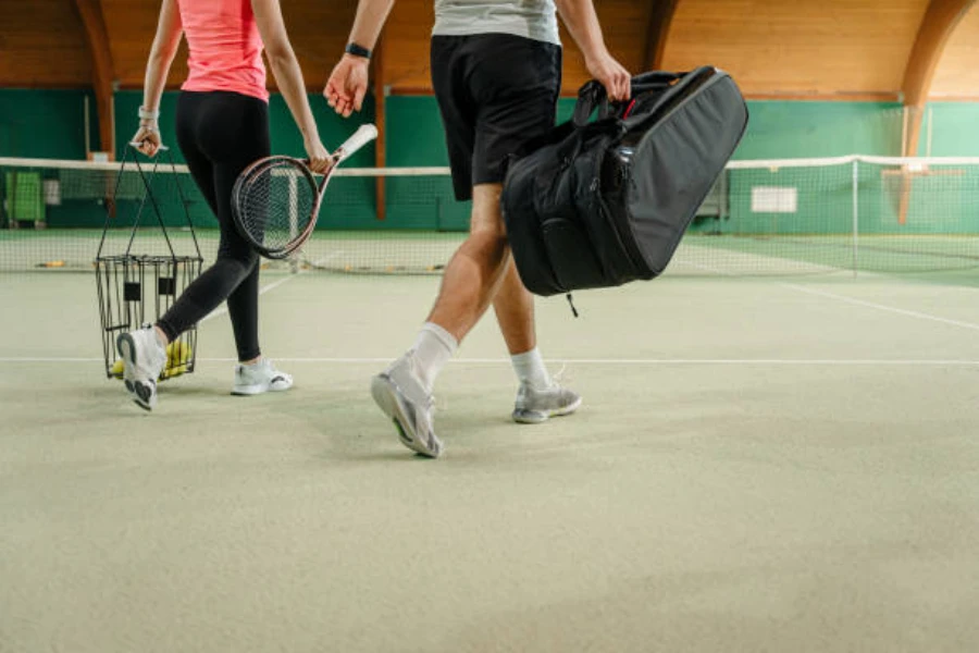 man walking with black 6 racket tennis bag on court