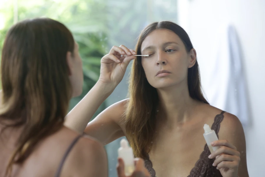 person applying eyelash serum in the mirror