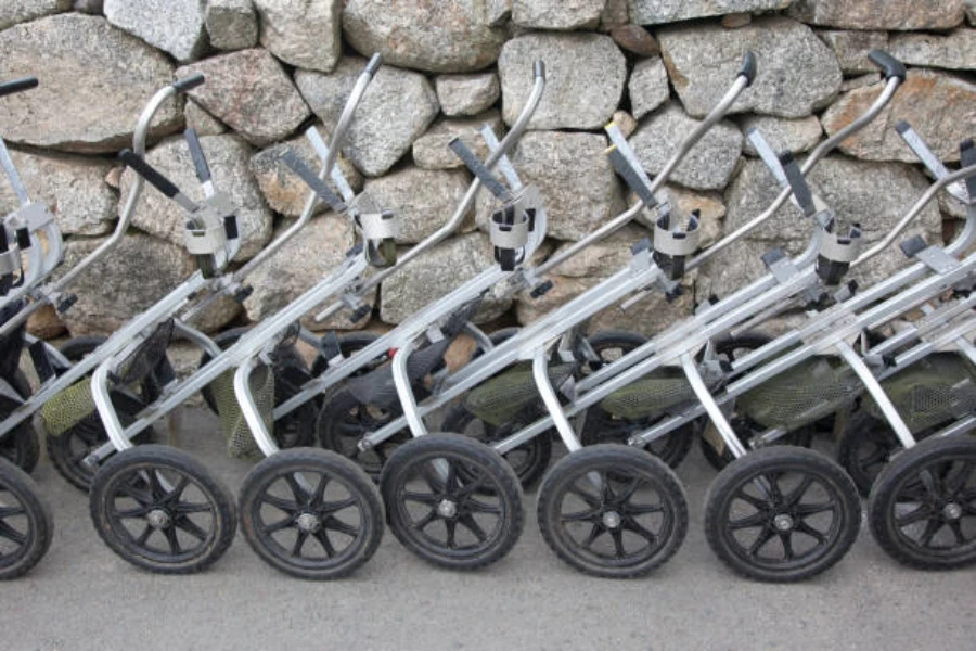 Row of silver golf trolleys lined up against stone wall