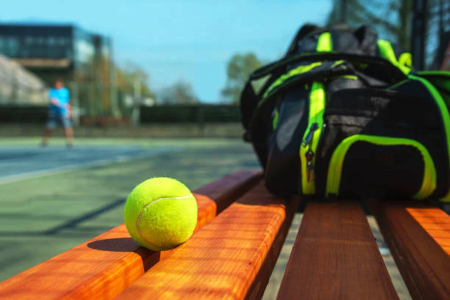 tennis ball on bench sitting next to racket bag