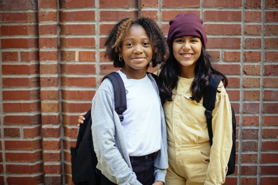 Two smiling girls standing side by side wearing bookbags