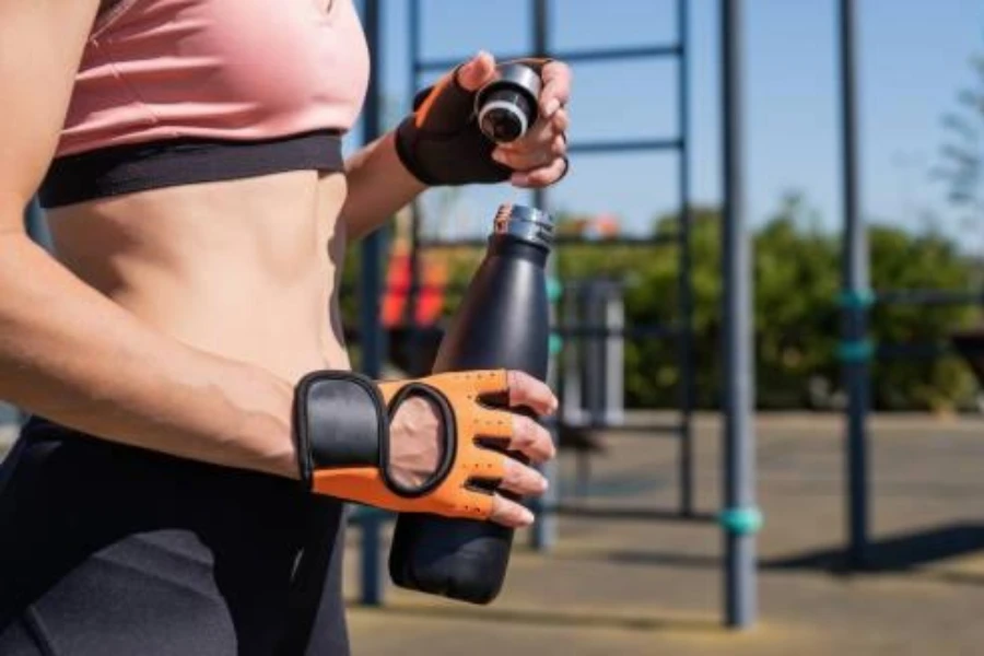 woman with orange gloves holding an insulated sports water bottle