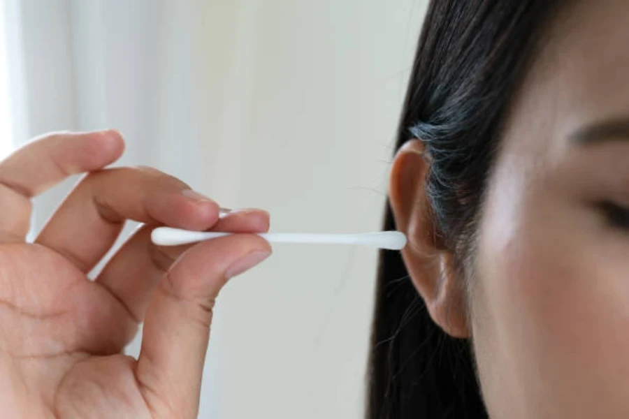 Mujer joven usando un bastoncillo de algodón para su oreja