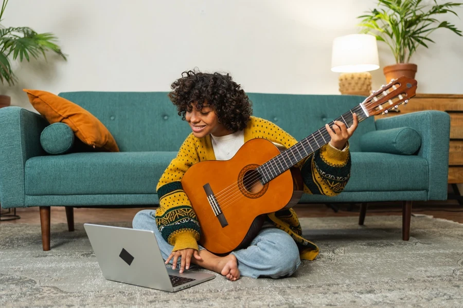 African woman sitting on floor with laptop for guitar lessons