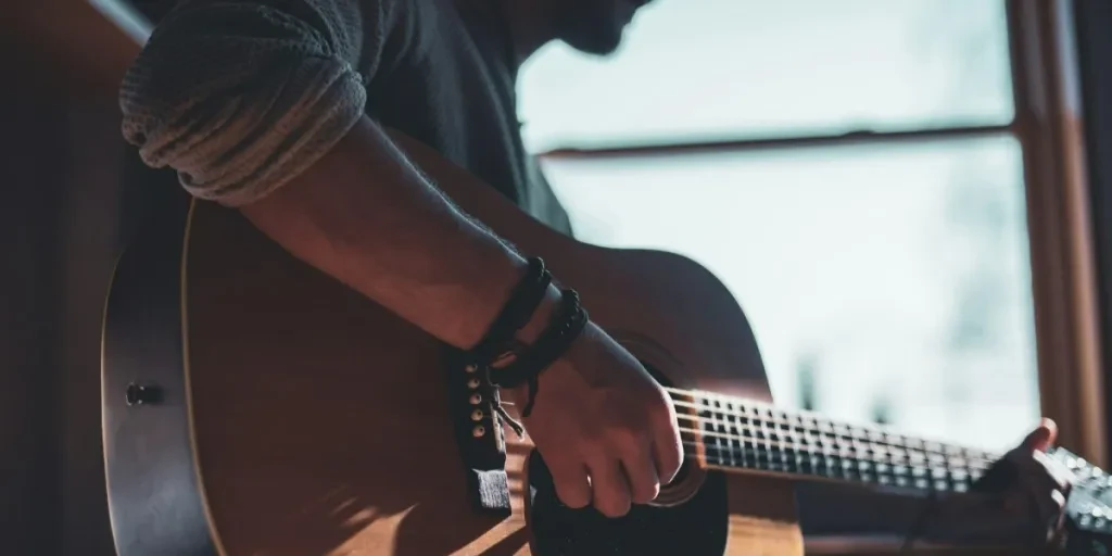 Man playing acoustic guitar while sitting next to window