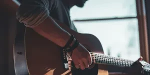Man playing acoustic guitar while sitting next to window