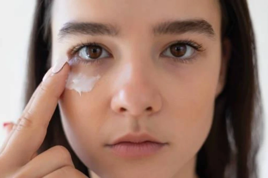 A close-up image of young lady applying eye cream