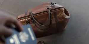 A leather bag on the floor with a person holding a passport above it