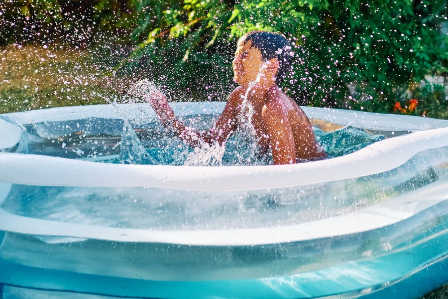 A little boy splashing in a clear blue inflatable pool in a backyard