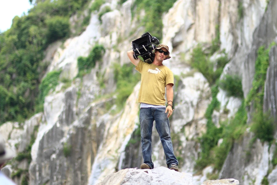 A man standing on a boulder with heavy camera on one shoulder