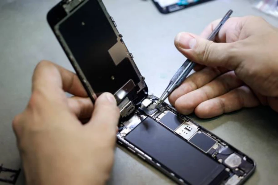 A man using fine-tipped curved tweezers to disassemble a phone