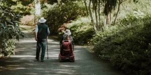 A man walking alongside a woman on a mobility scooter