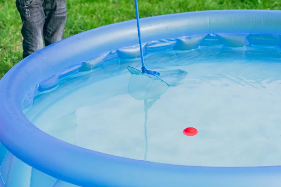 Una persona que utiliza un skimmer azul para limpiar una piscina inflable.