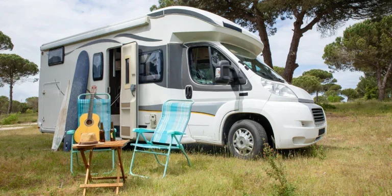 A recreational vehicle parked in a park with chairs outside