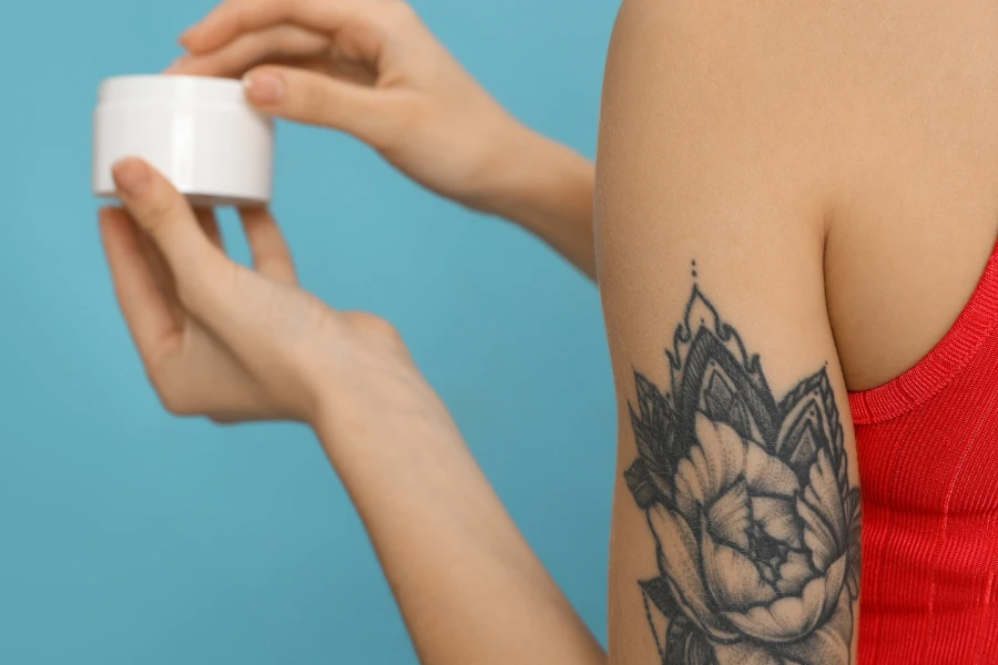 A tattooed woman holding a tattoo cream
