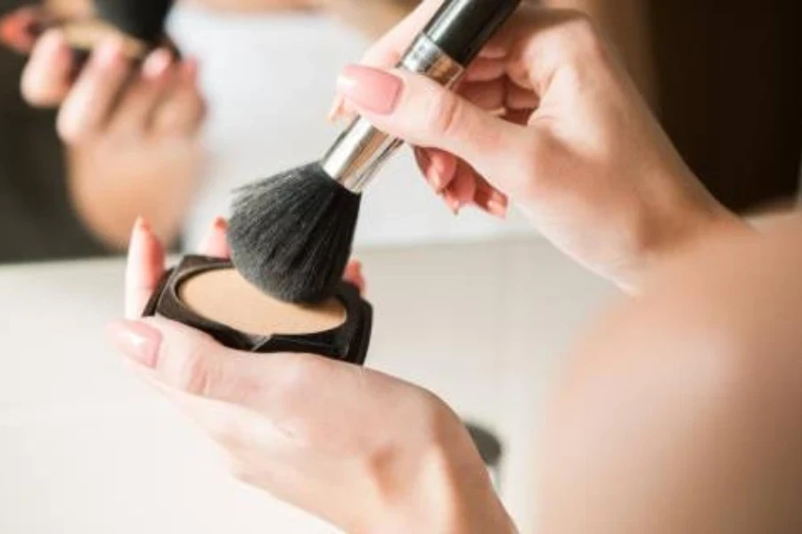 Una mujer usando una brocha de belleza con maquillaje en polvo.