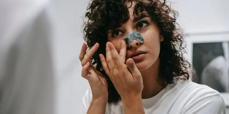 A young lady laying a nose strip on her nose