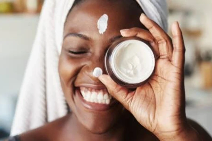 Une jeune femme souriant tout en tenant un petit récipient de crème hydratante