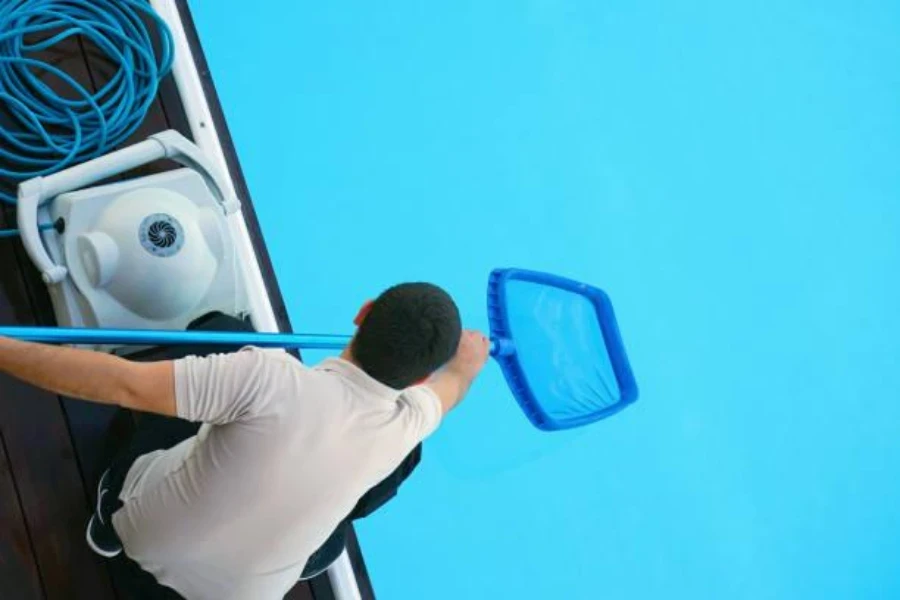 A young man cleaning pool with a skimmer net