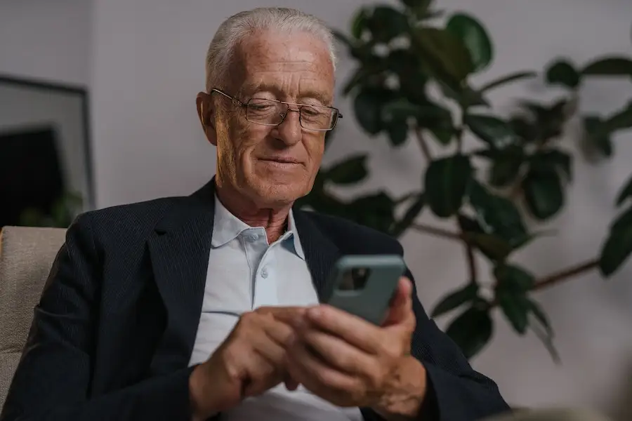An elderly man wearing eyeglasses while using his mobile phone