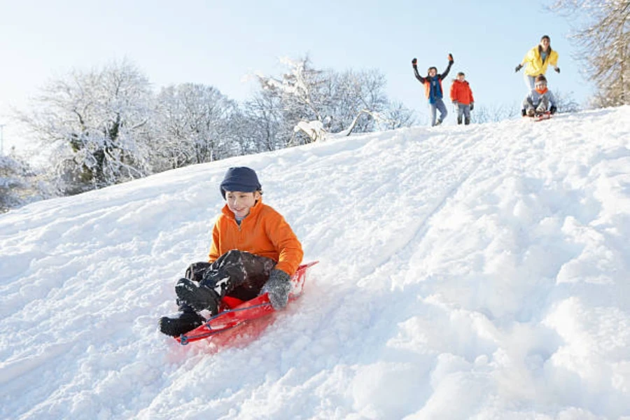 Ragazzo che scende dalla collina innevata su una piccola slitta di plastica rossa