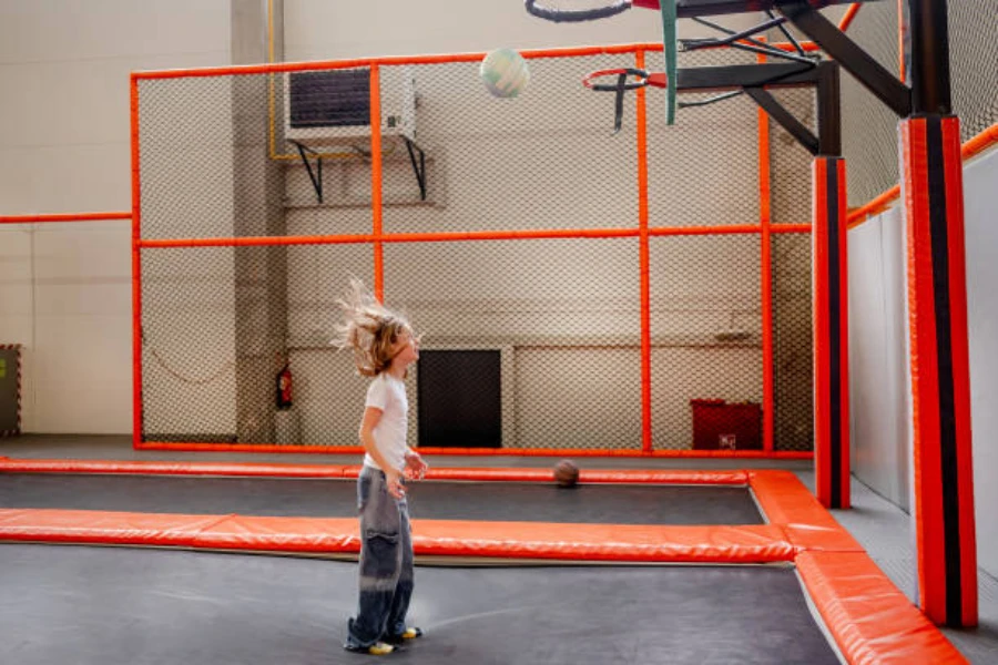 Child on a rectangular trampoline with a basketball hoop indoors