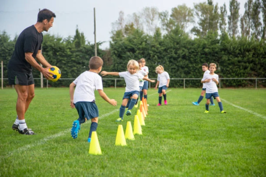 Niños usando conos de agilidad amarillos durante el entrenamiento de fútbol al aire libre